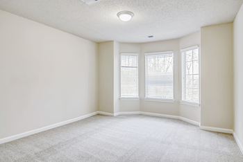 an empty bedroom with three windows and a carpeted floor